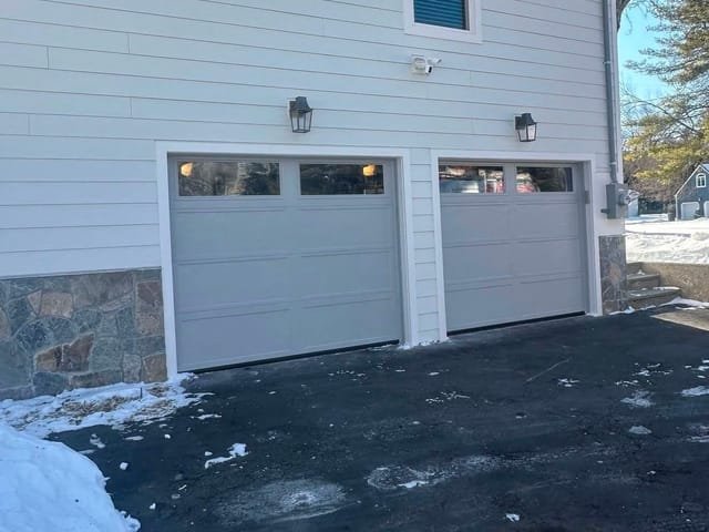 Two matching light-gray carriage-style garage doors with windows on a home with a stone base
